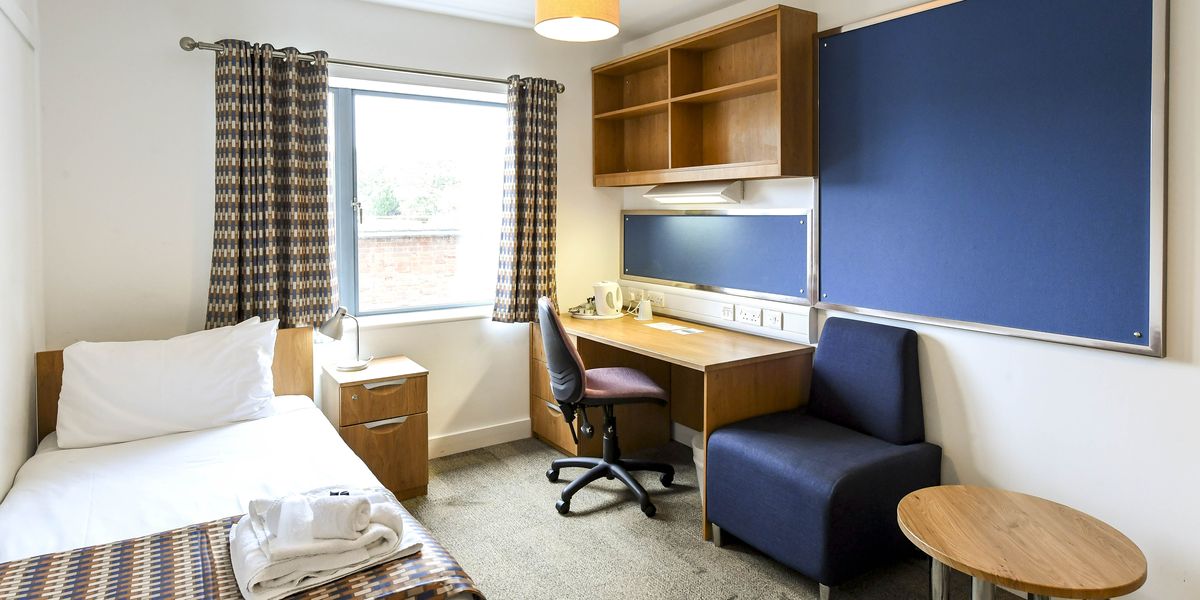 A single en-suite room at Selwyn College, with a bed, a desk and an armchair
