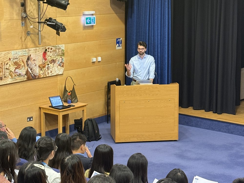 Students with handouts listen to a speaker at the lectern in a lecture theatre