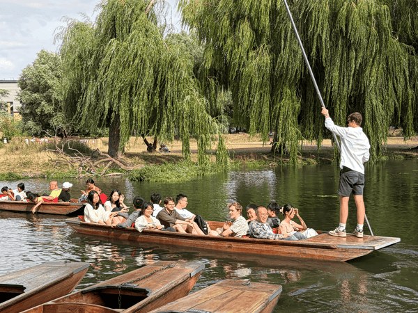 Students in a punt on the river, with willow trees on the bank