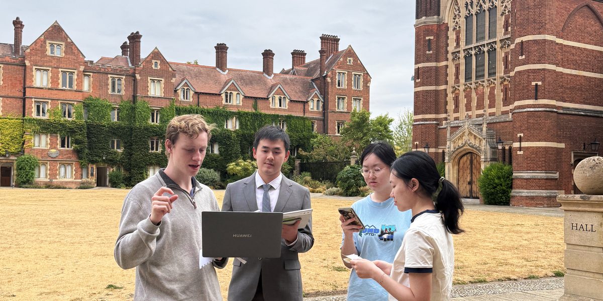 Three students and a teacher look at a laptop in a court at Selwyn College