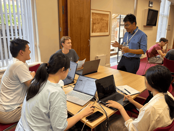 A teacher talks with students working at their laptops
